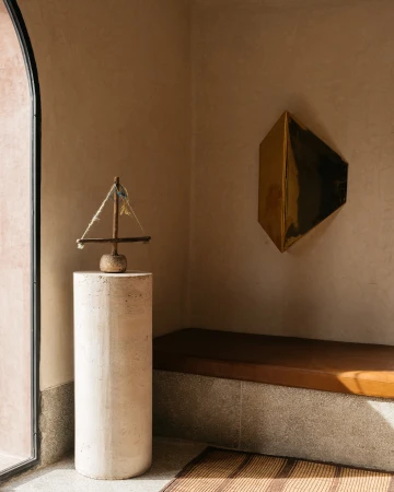Interior view with decorative sailboat sculpture atop a cylindrical plinth, set against a backdrop of textured walls and modern art.