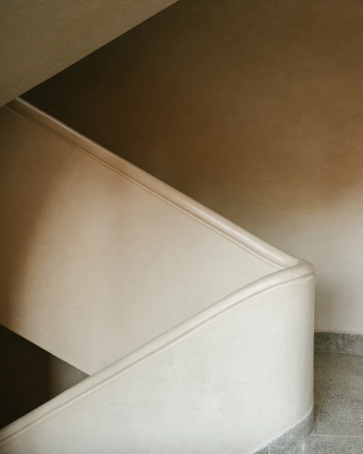 Architectural shot of a curved, off-white stairway with a minimalist aesthetic, highlighting interior design and the play of light and shadow.