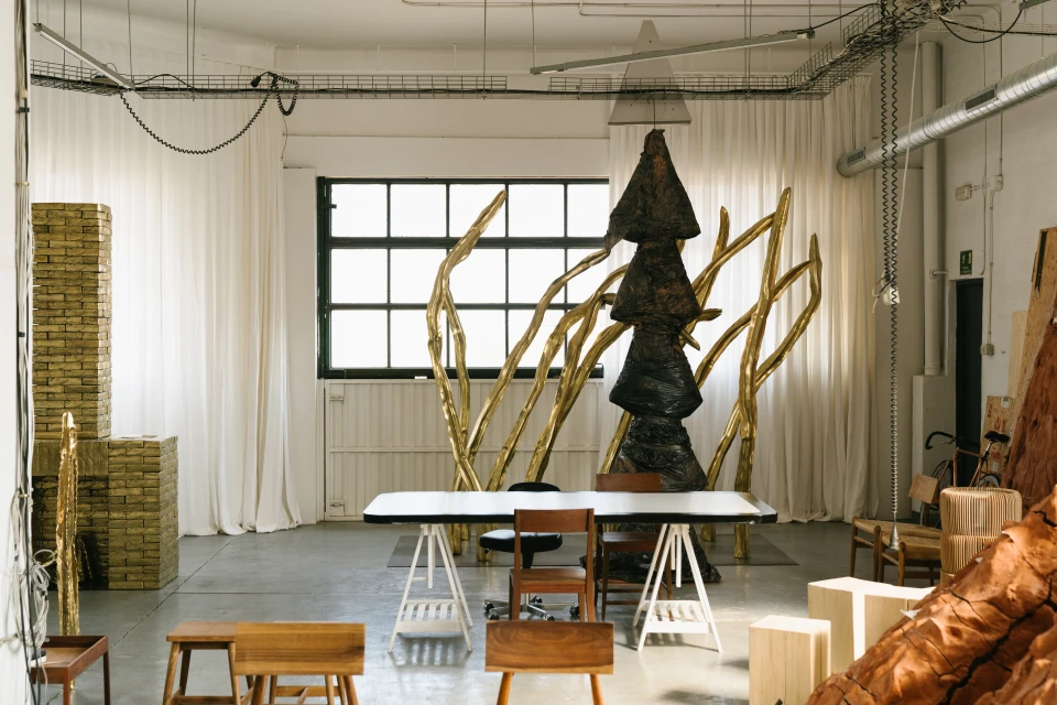 Industrial-style room featuring a sculpture, table, chairs, and natural light through a window, creating an artistic and functional space.
