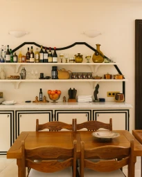 Wooden dining table and chairs in front of a white built-in bar counter with display shelves of wine bottles and glassware.