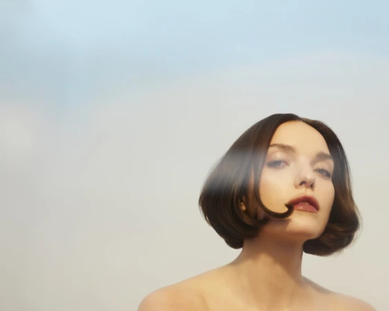 Portrait of a woman with short brunette hair and bare shoulders against a soft background. Light from an unseen source highlights her facial features.