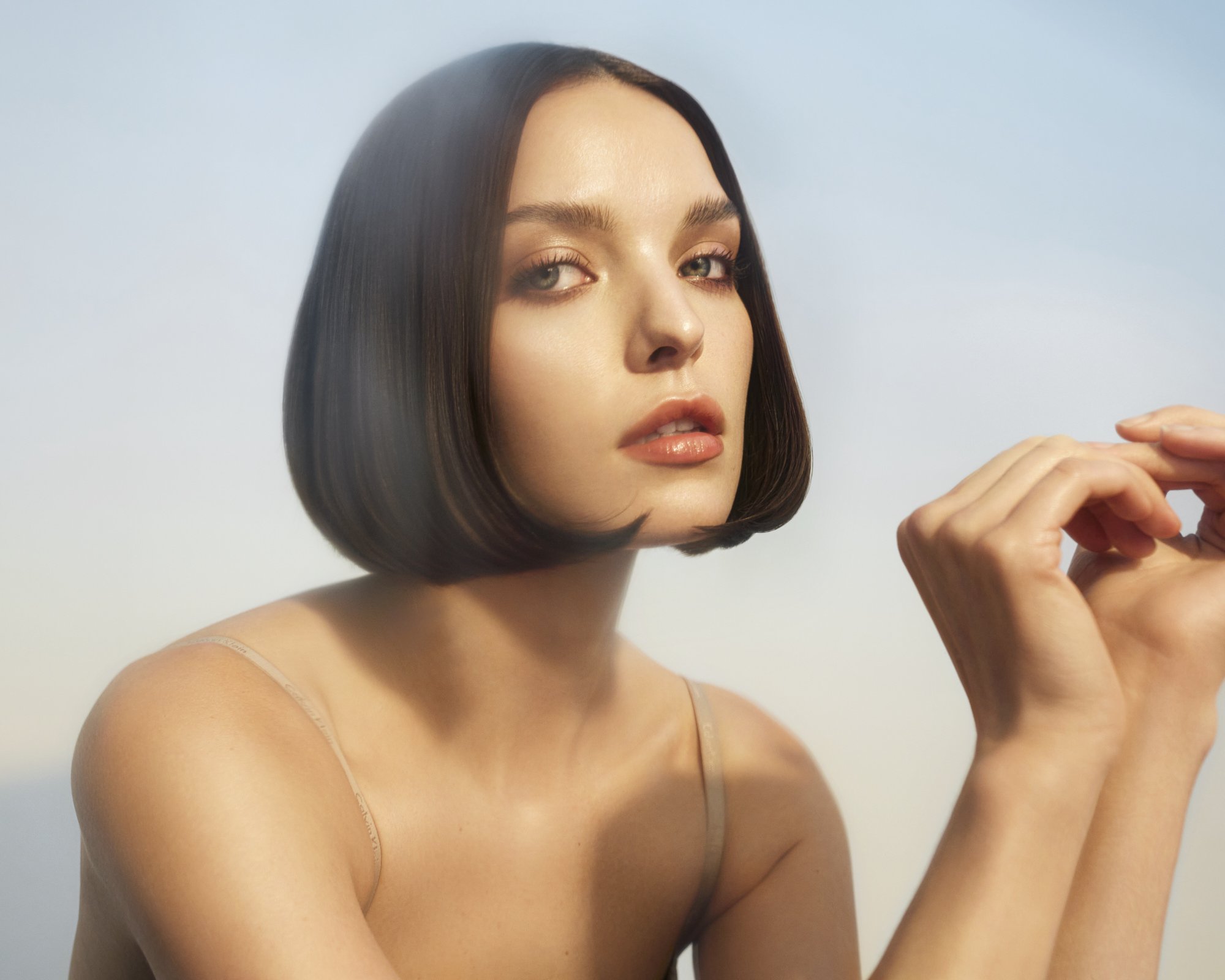 Portrait of a young adult woman with bob hairstyle and nude top, posing in a bright studio environment with diffused lighting.