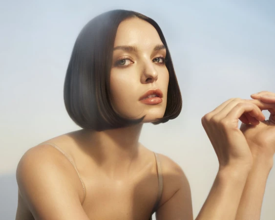 Portrait of a young adult woman with bob hairstyle and nude top, posing in a bright studio environment with diffused lighting.