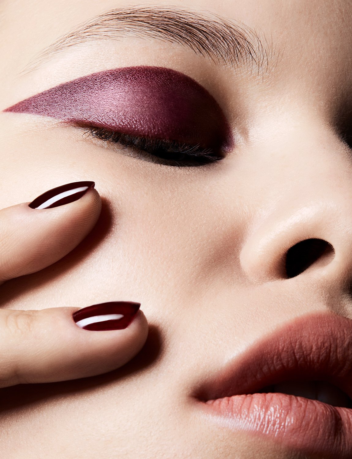 Close-up of a woman's face with burgundy eyeshadow and matching manicure. Beauty shot highlighting makeup and nail color.