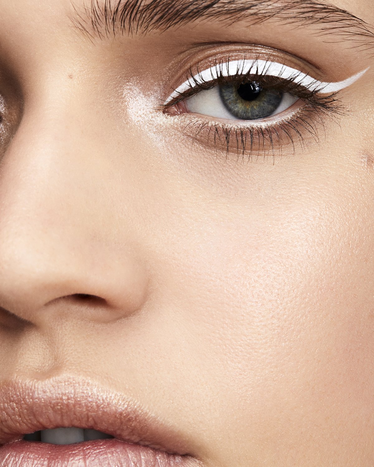 Close-up studio shot of a woman's face with fair skin, light eyebrows, and a bold white eyeliner winged beauty makeup look.