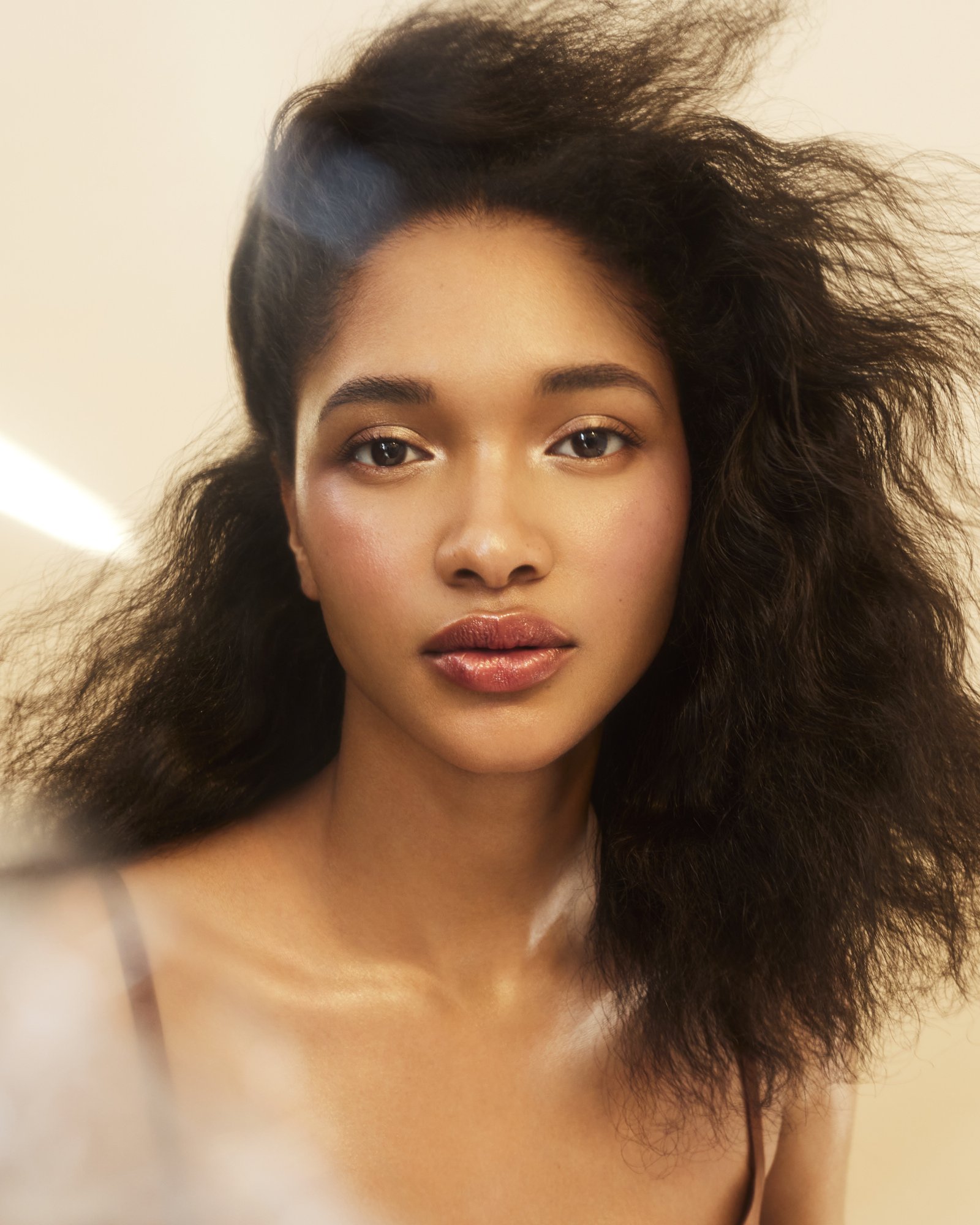 Close-up portrait of a young woman with dark curly hair, soft makeup, and natural lighting. Beauty and fashion portrait photography.
