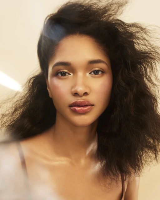 Close-up portrait of a young woman with dark curly hair, soft makeup, and natural lighting. Beauty and fashion portrait photography.