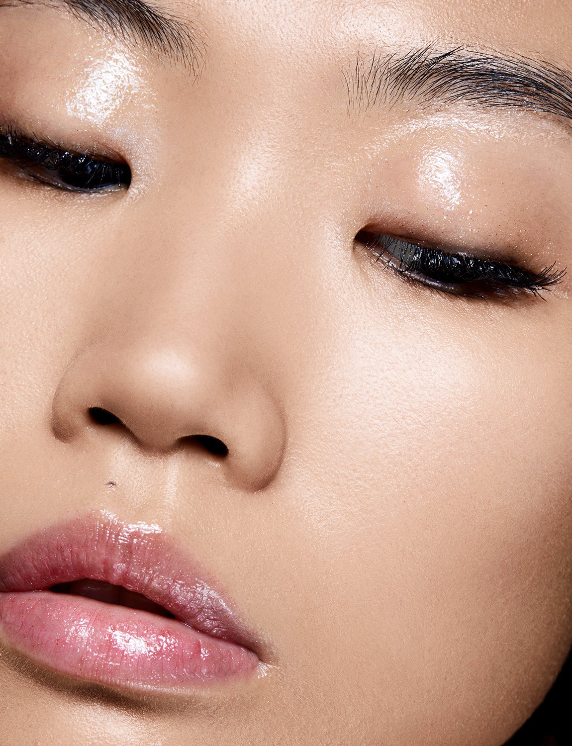 Close-up portrait of an adult woman with closed eyes and glossy lips, showcasing her facial features and skincare.