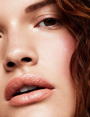 Extreme close-up macro portrait of a young woman's face showing dewy skin texture and glossy neutral lipstick.