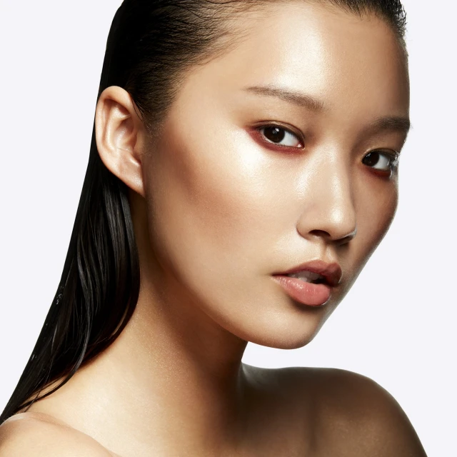 Close-up portrait of an Asian woman with glossy skin and wet-look hair, gazing at the camera against a stark white background in a beauty shot.