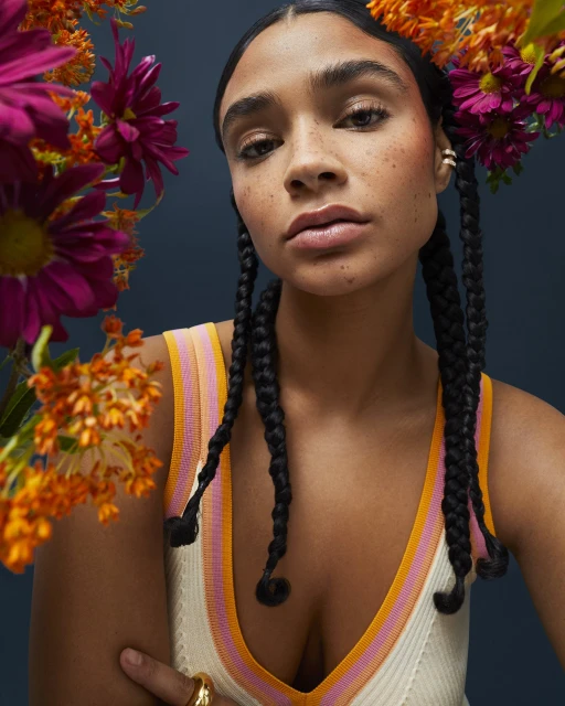 Portrait of woman with braided hair and fair skin in a striped knit top, surrounded by vibrant orange and magenta flowers.