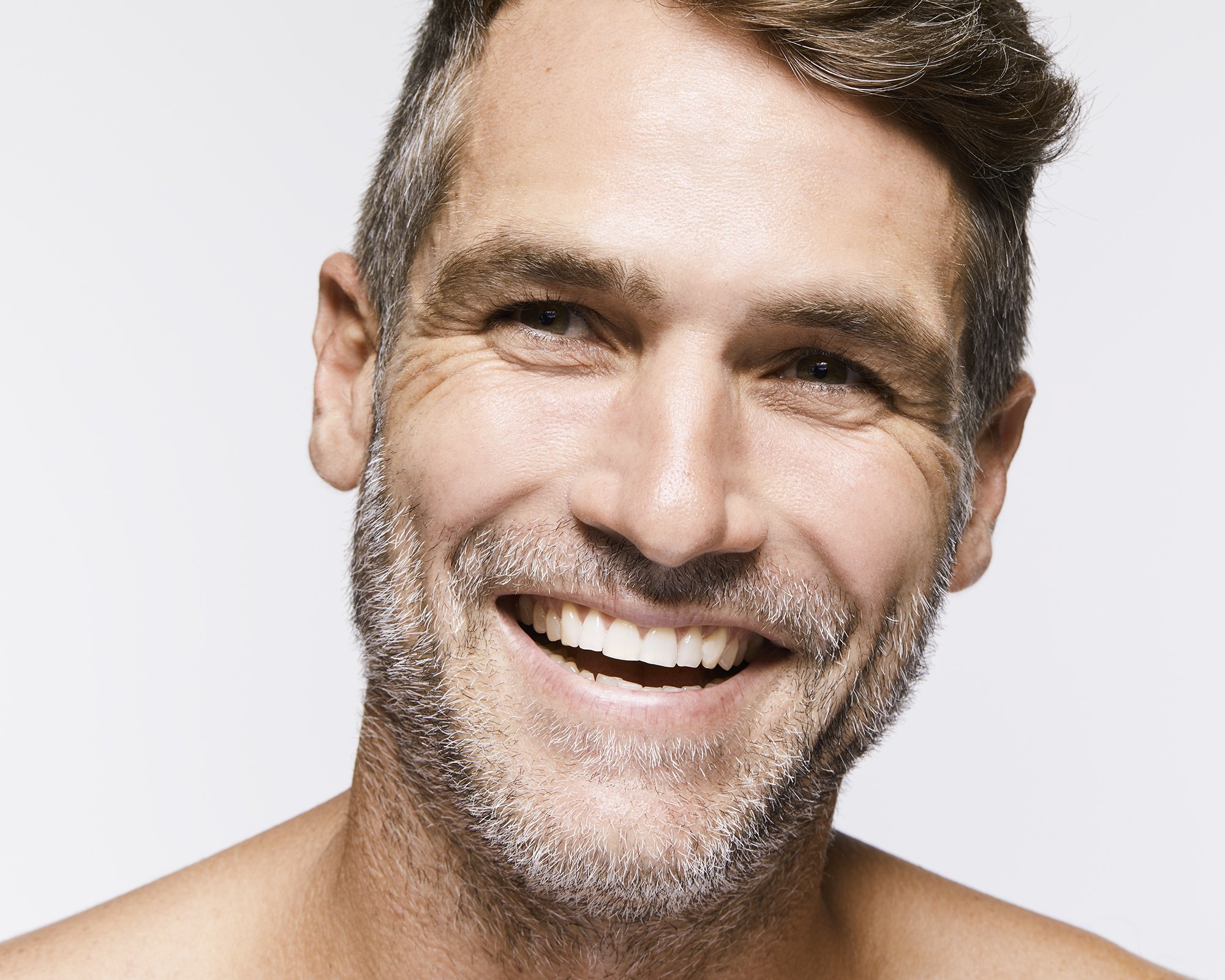 Close-up portrait of a smiling adult male with graying hair against a white background, showcasing genuine joy and positive expression.