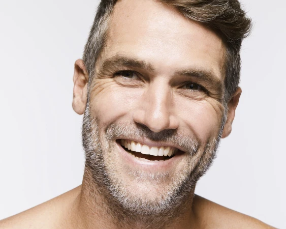 Close-up portrait of a smiling adult male with graying hair against a white background, showcasing genuine joy and positive expression.
