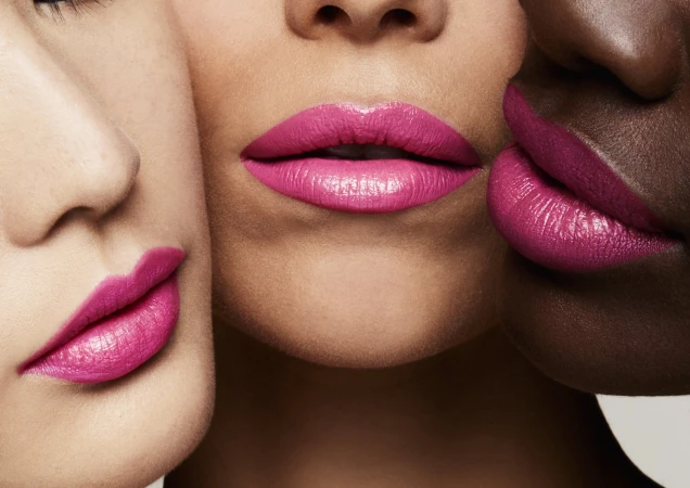 Close-up portrait of three women with diverse skin tones wearing vibrant pink and magenta lipstick against a neutral background.