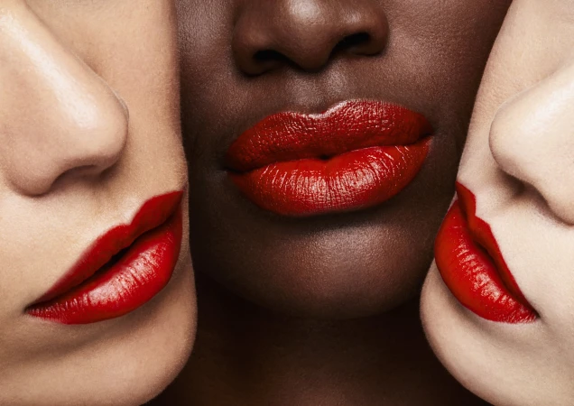 Close-up macro shot of three diverse models wearing vibrant red lipstick pressed closely together.