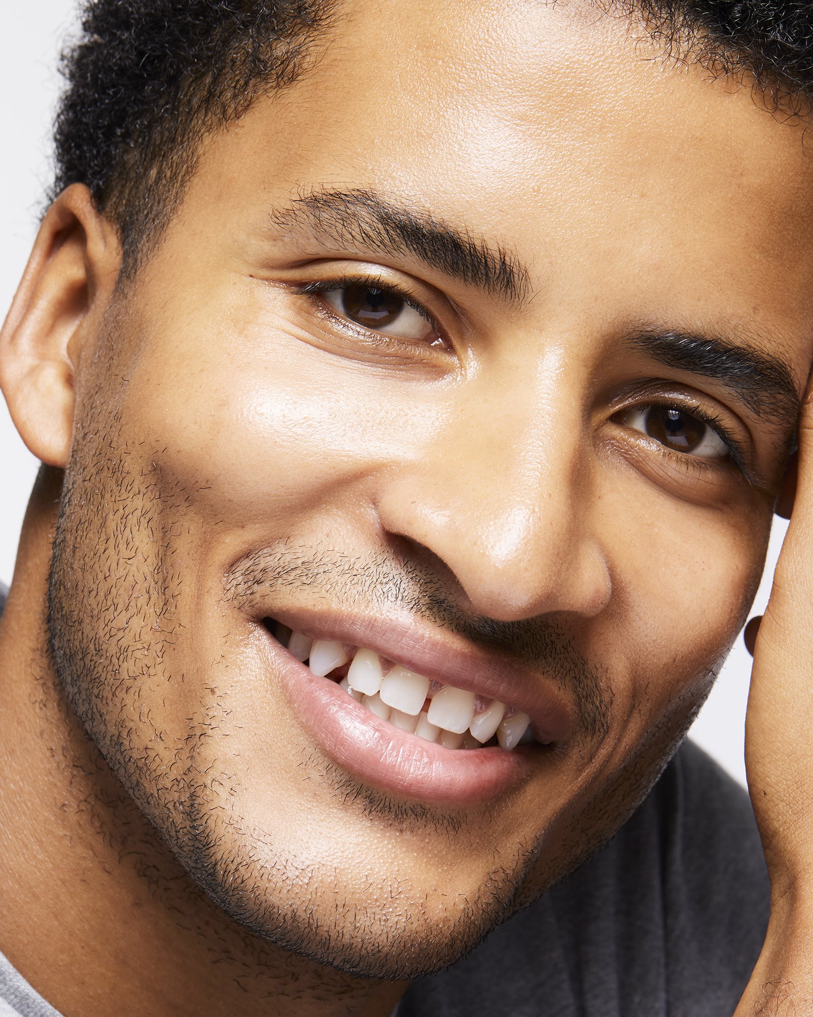 Close-up portrait of a smiling Black man with short dark hair and facial stubble against a white background