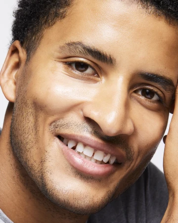 Close-up portrait of a smiling Black man with short dark hair and facial stubble against a white background