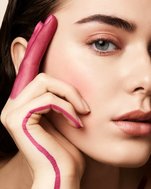 Close-up studio shot of a light-skinned woman's face and hand, partly painted in fuchsia, showcasing beauty and artistic expression.