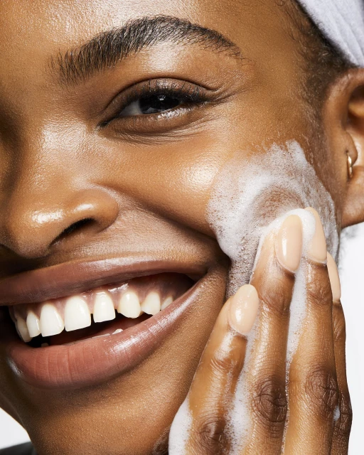 Close-up of a smiling adult woman washing her face with foamy cleanser, showcasing skincare, beauty, wellness, and personal care routine.