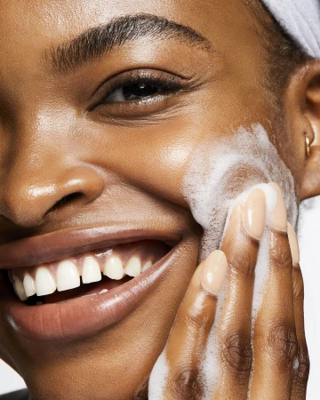 Close-up of a smiling adult woman washing her face with foamy cleanser, showcasing skincare, beauty, wellness, and personal care routine.