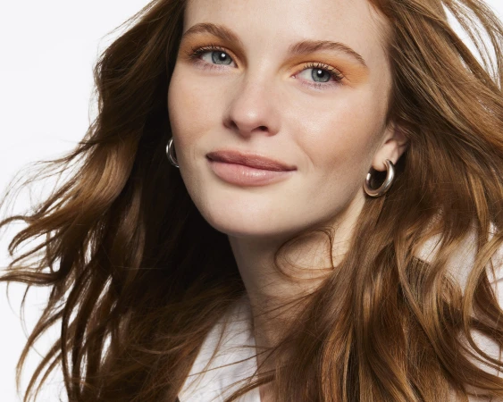Close-up portrait of a woman with red hair and warm orange eye shadow wearing silver hoop earrings