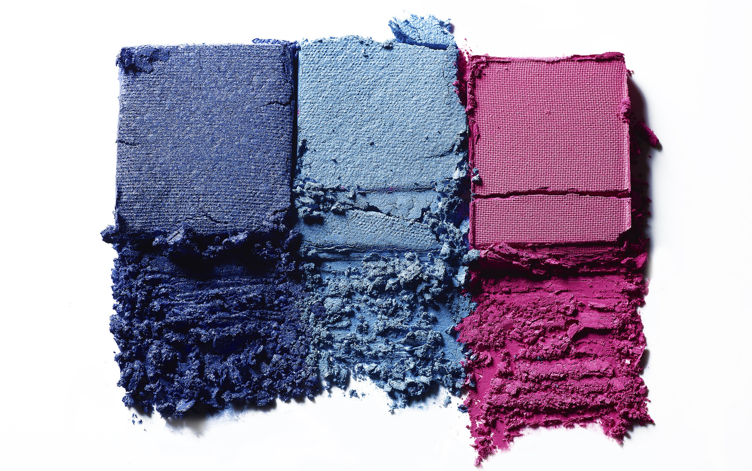 Closeup of vibrant eyeshadow swatches in blue, light blue, and pink on a white background, displaying color and texture.