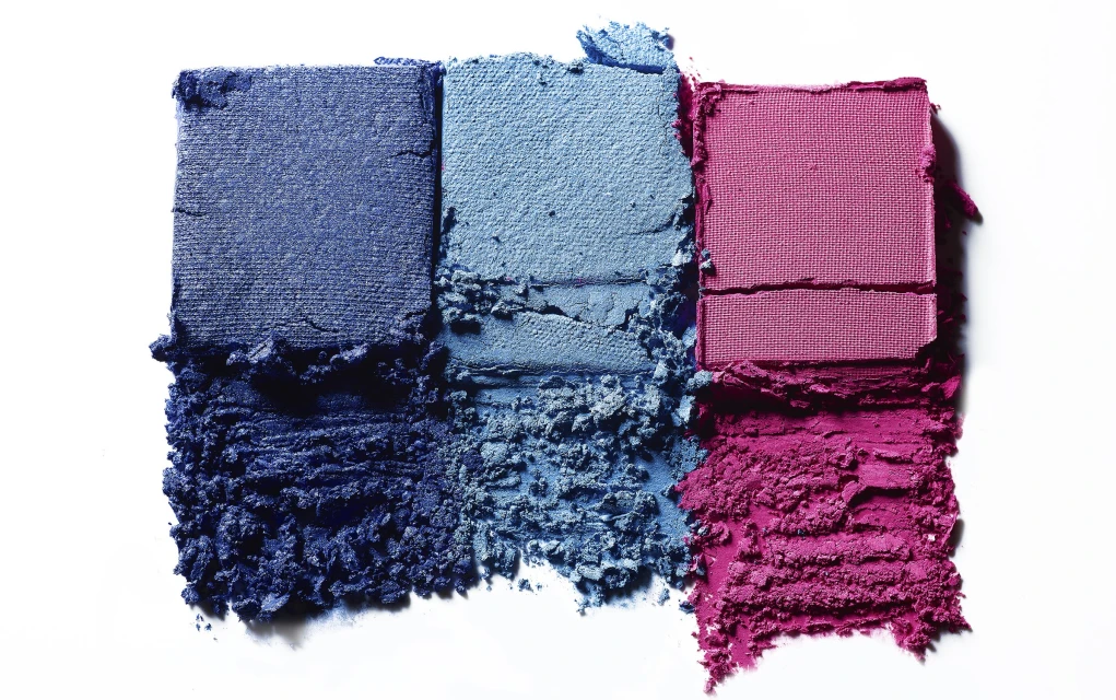 Closeup of vibrant eyeshadow swatches in blue, light blue, and pink on a white background, displaying color and texture.