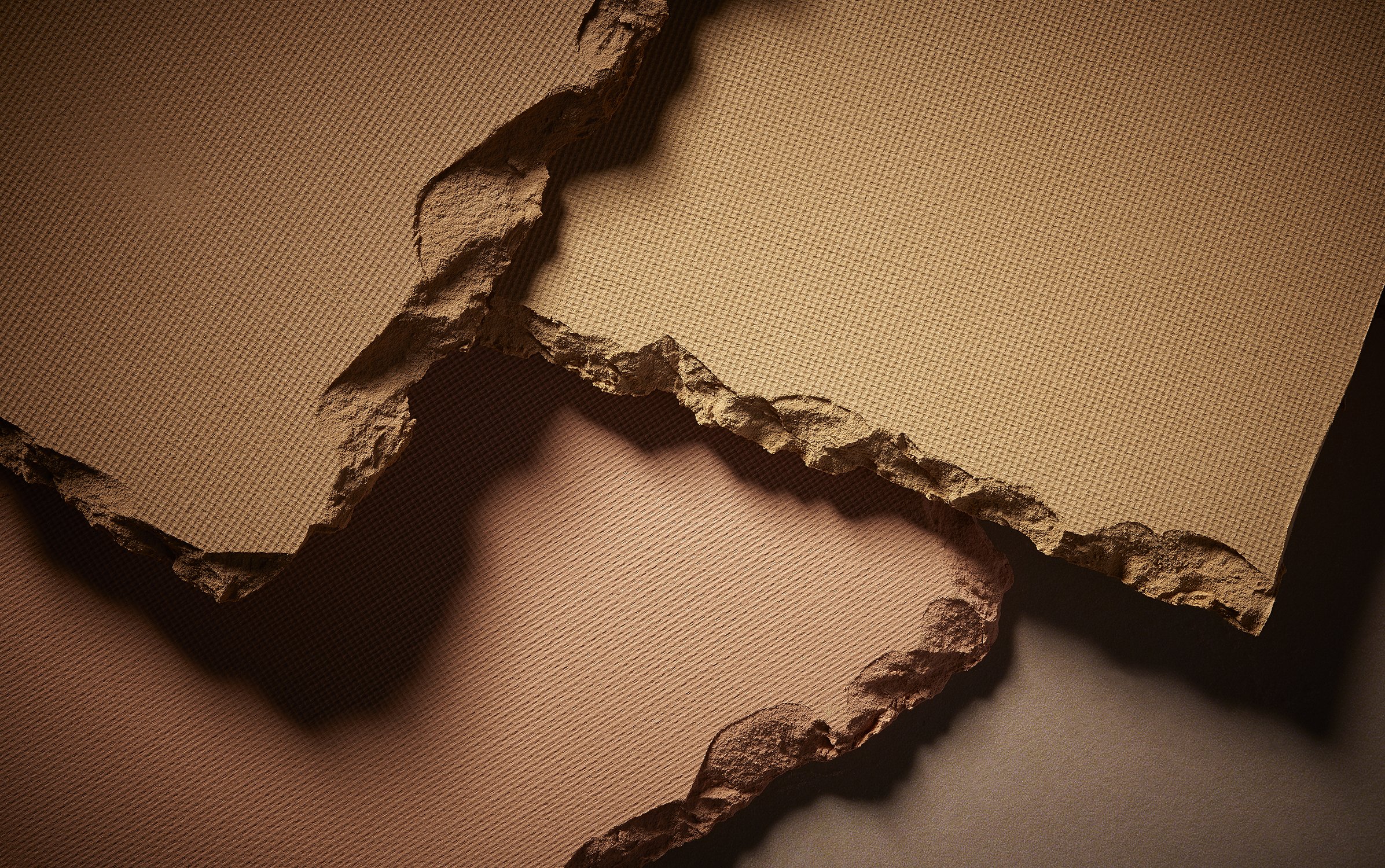 Close-up macro shot of layered torn textured paper with ragged edges in neutral beige and tan tones.