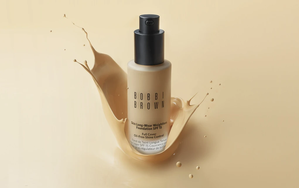 Bobbi Brown Skin Long-Wear Weightless Foundation SPF 15 bottle on a beige background with splash of liquid foundation.
