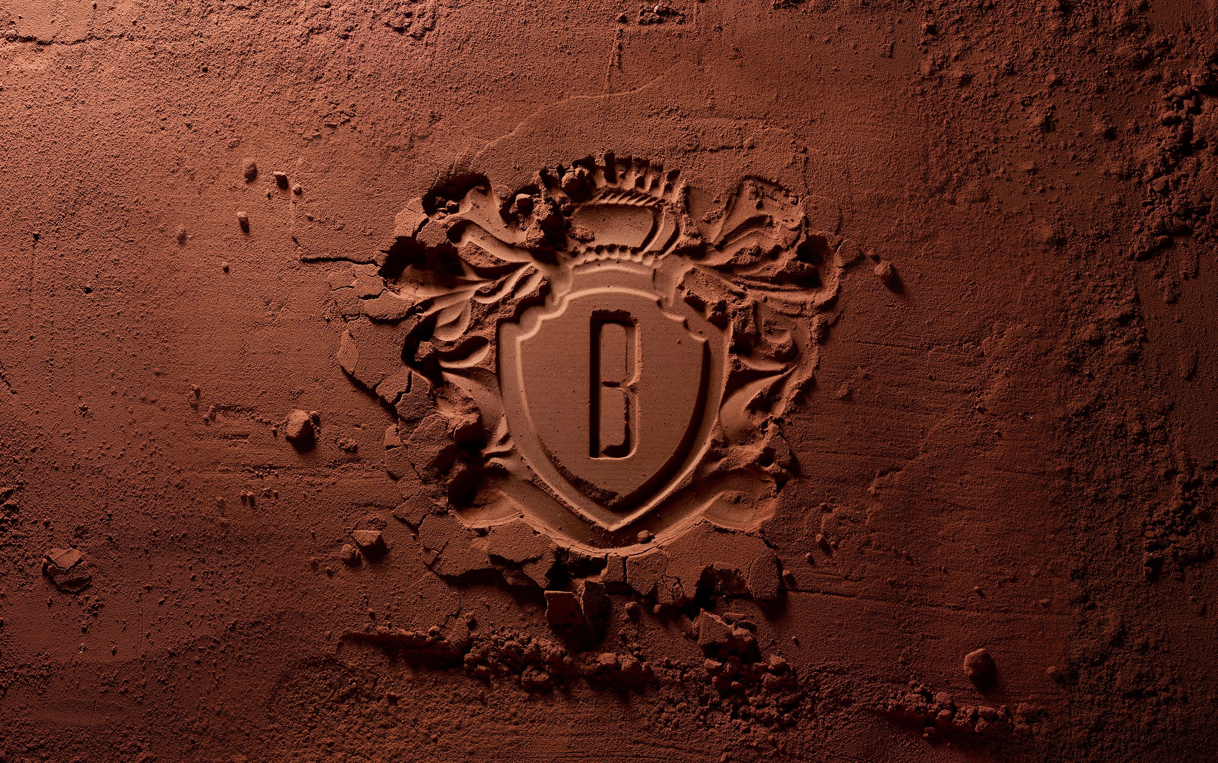 Embossed chocolate powder with a royal crest design featuring the letter B in the center, creating a visually rich and textured image.