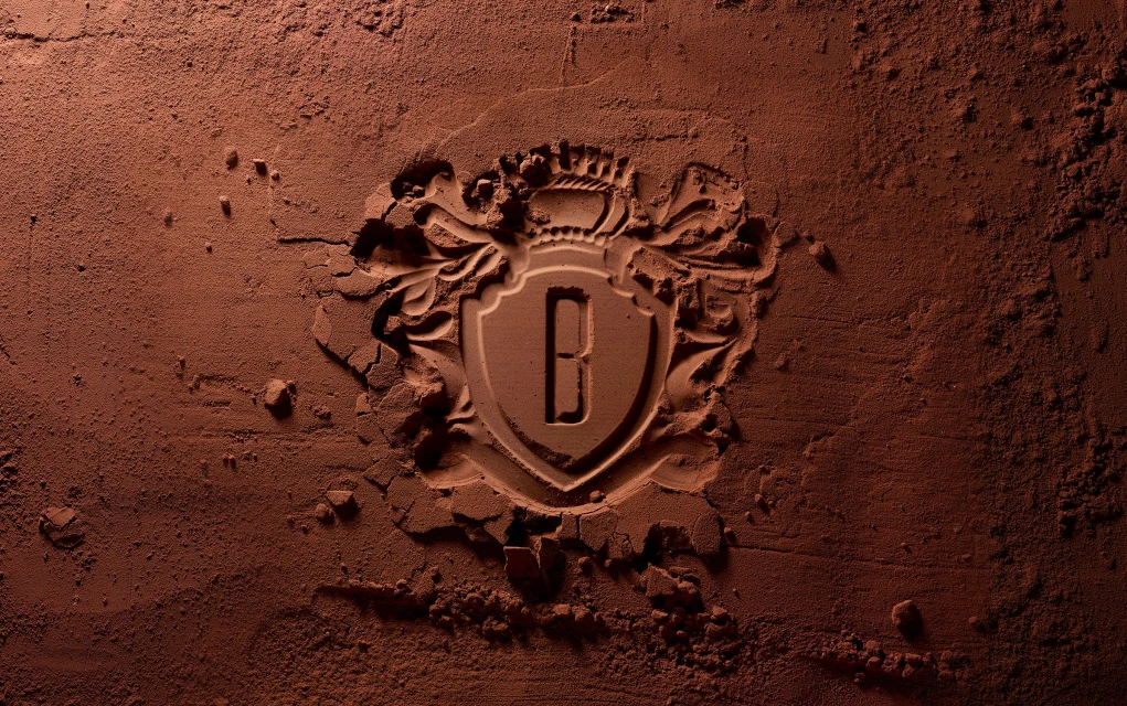 Embossed chocolate powder with a royal crest design featuring the letter B in the center, creating a visually rich and textured image.