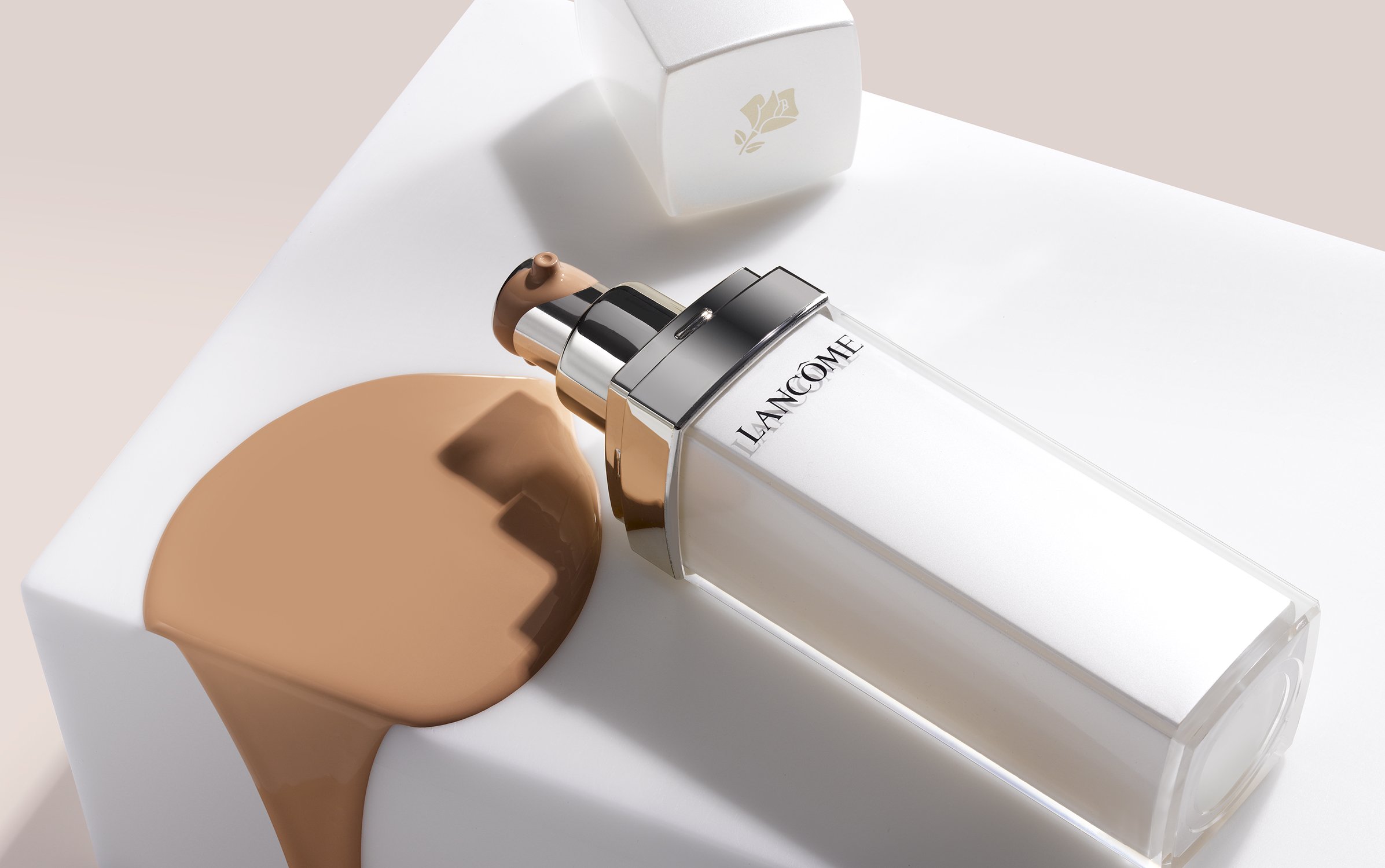 Lancôme skincare product bottle with foundation makeup on a white surface. Close-up shot of a beauty product in a studio setting.
