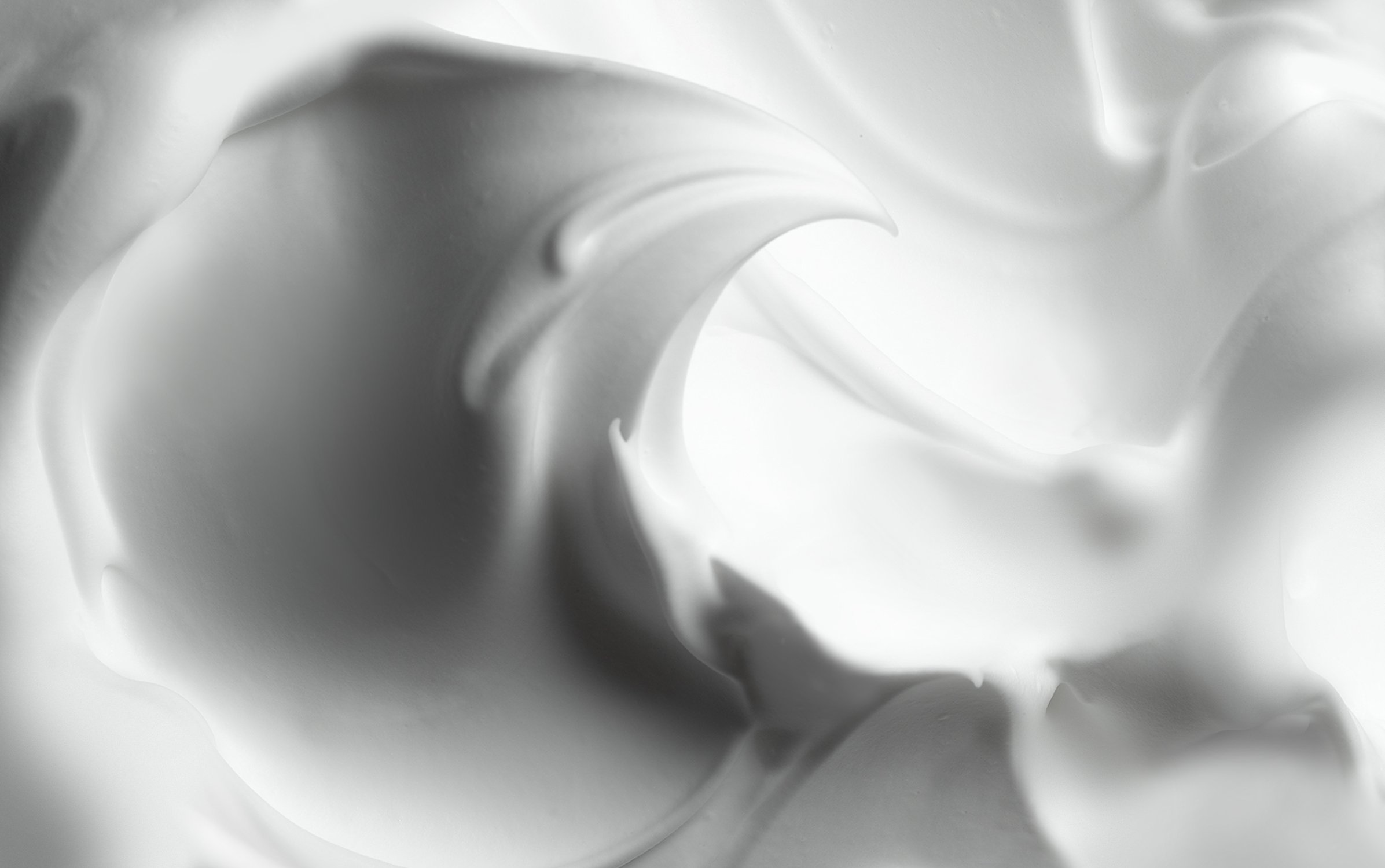 Macro view of smooth white cream showing soft curving ridges and velvety foam texture in monochrome lighting