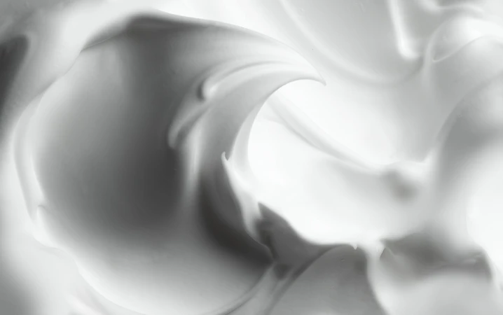 Macro view of smooth white cream showing soft curving ridges and velvety foam texture in monochrome lighting