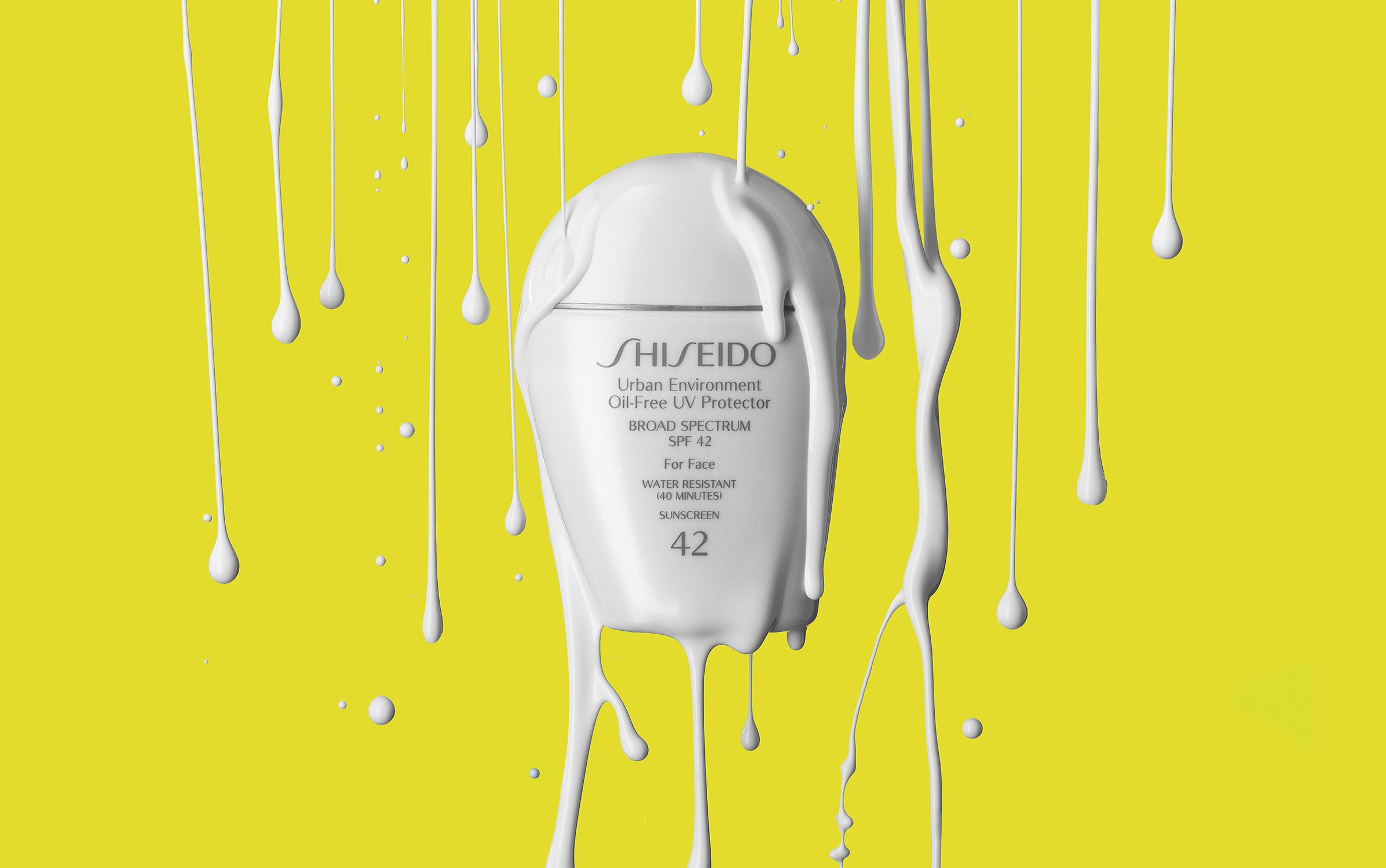 Promotional shot of Shiseido Urban Environment Oil-Free UV Protector SPF 42 sunscreen bottle covered in white liquid against yellow background.