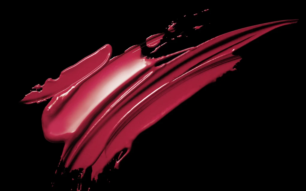 Macro shot of a swipe of glossy red lipstick with visible brushstrokes against a stark black background, showcasing texture and color.