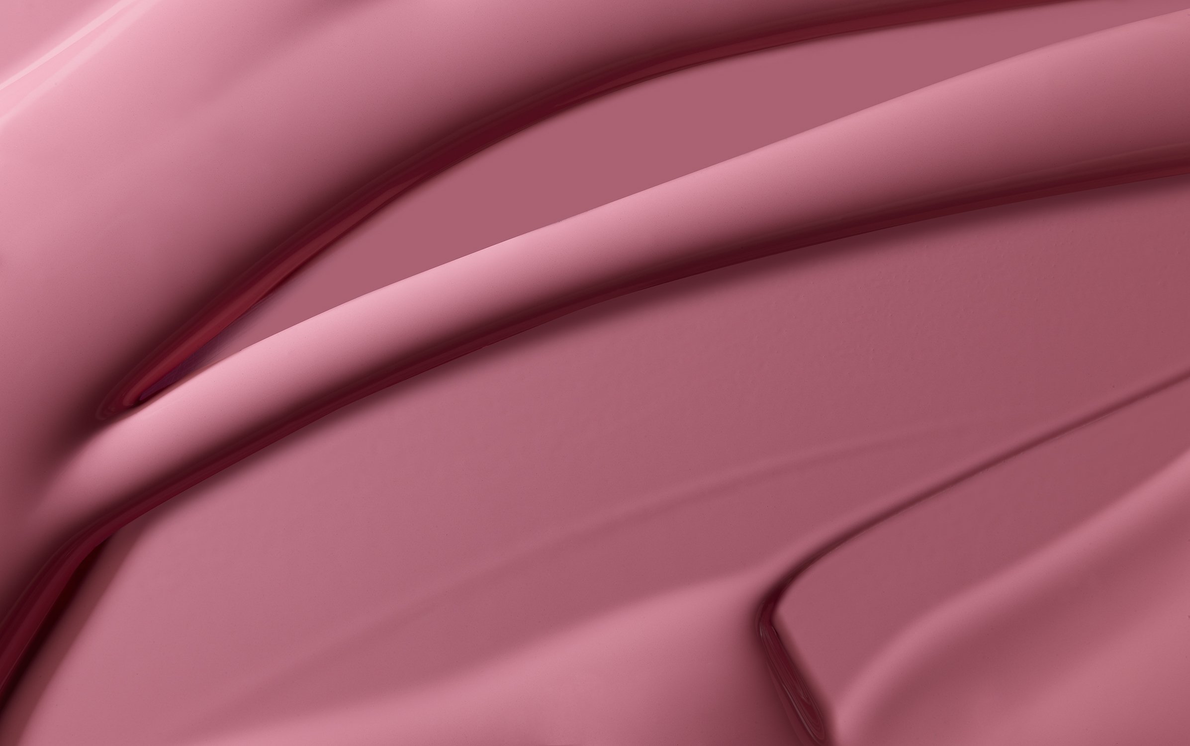 Abstract close-up shot of textured, glossy makeup in a solid color of rose pink, with swirling, rounded linear patterns and shadows.