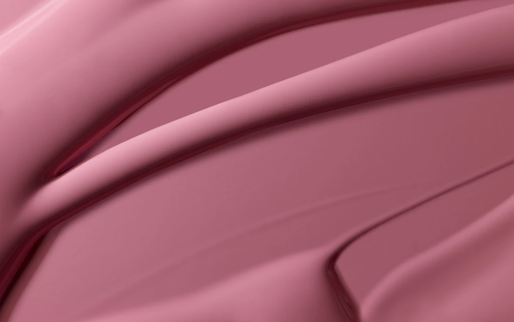 Abstract close-up shot of textured, glossy makeup in a solid color of rose pink, with swirling, rounded linear patterns and shadows.