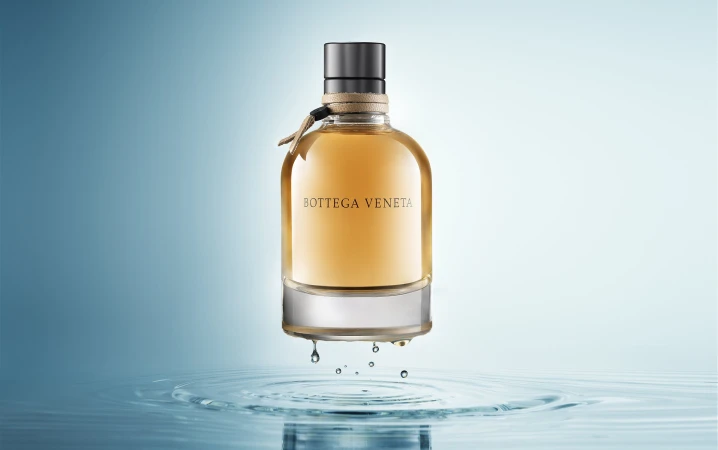 Bottega Veneta perfume bottle levitating above water ripples against a blue gradient backdrop
