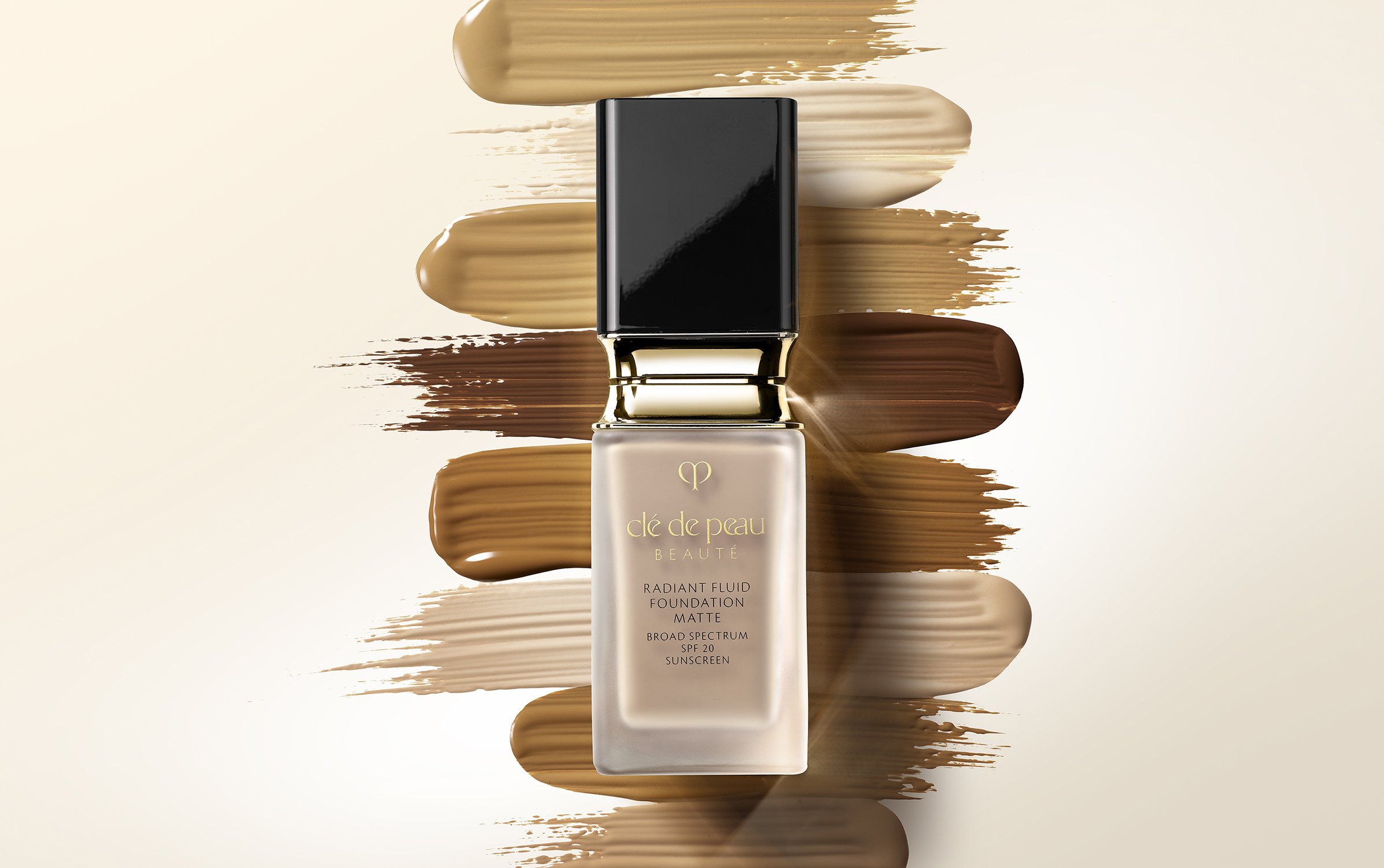 Cosmetic foundation bottle displayed alongside swatches of different shades, set against a soft, gradient background. Beauty product shot.