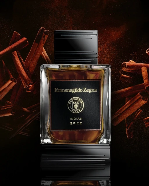 Ermenegildo Zegna Indian Spice perfume bottle on a black surface surrounded by cinnamon sticks, showcasing fragrance and presentation.