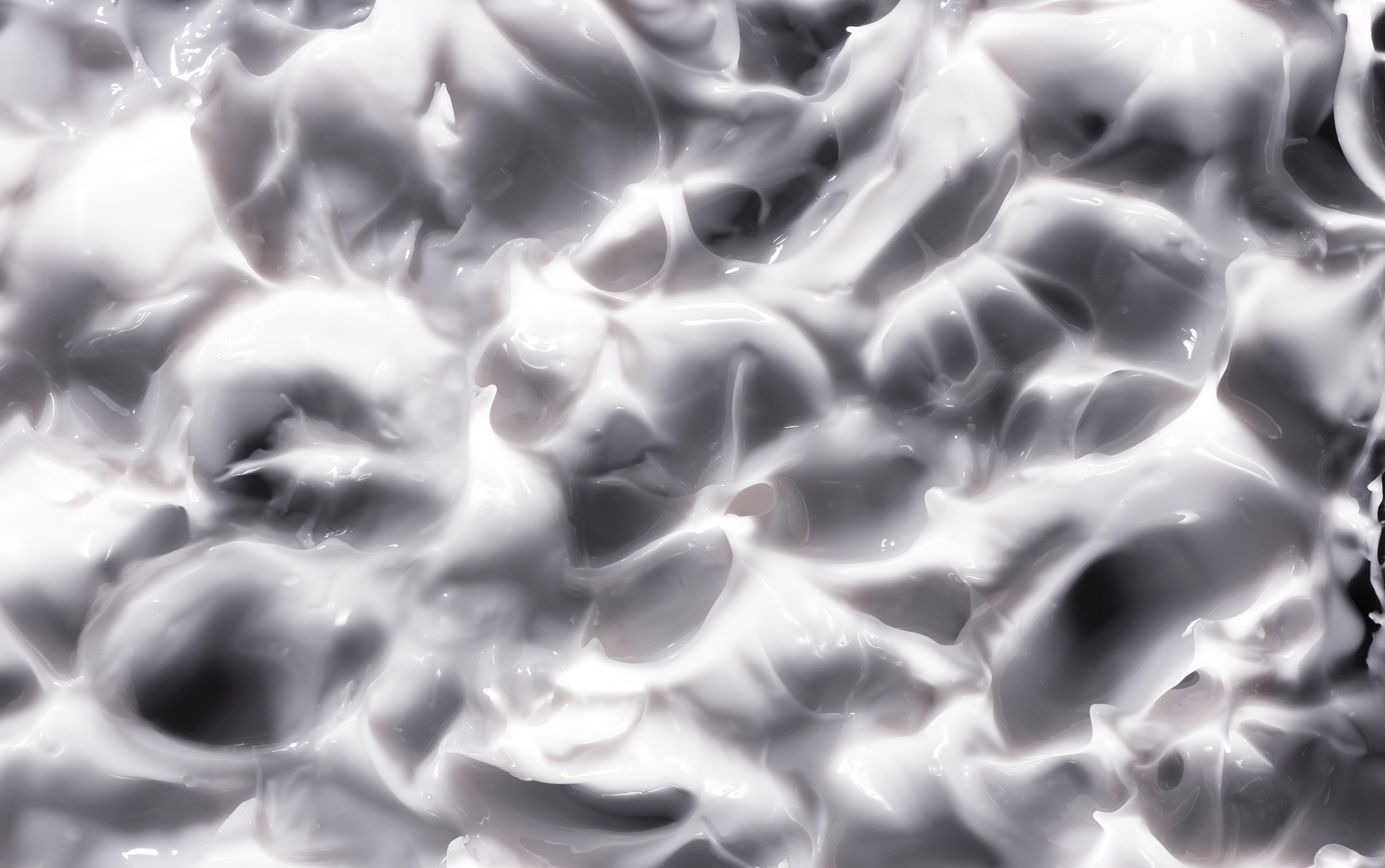 Close-up of thick white cream texture with swirls and shadows, illuminated by bright light, for beauty and skincare concepts.
