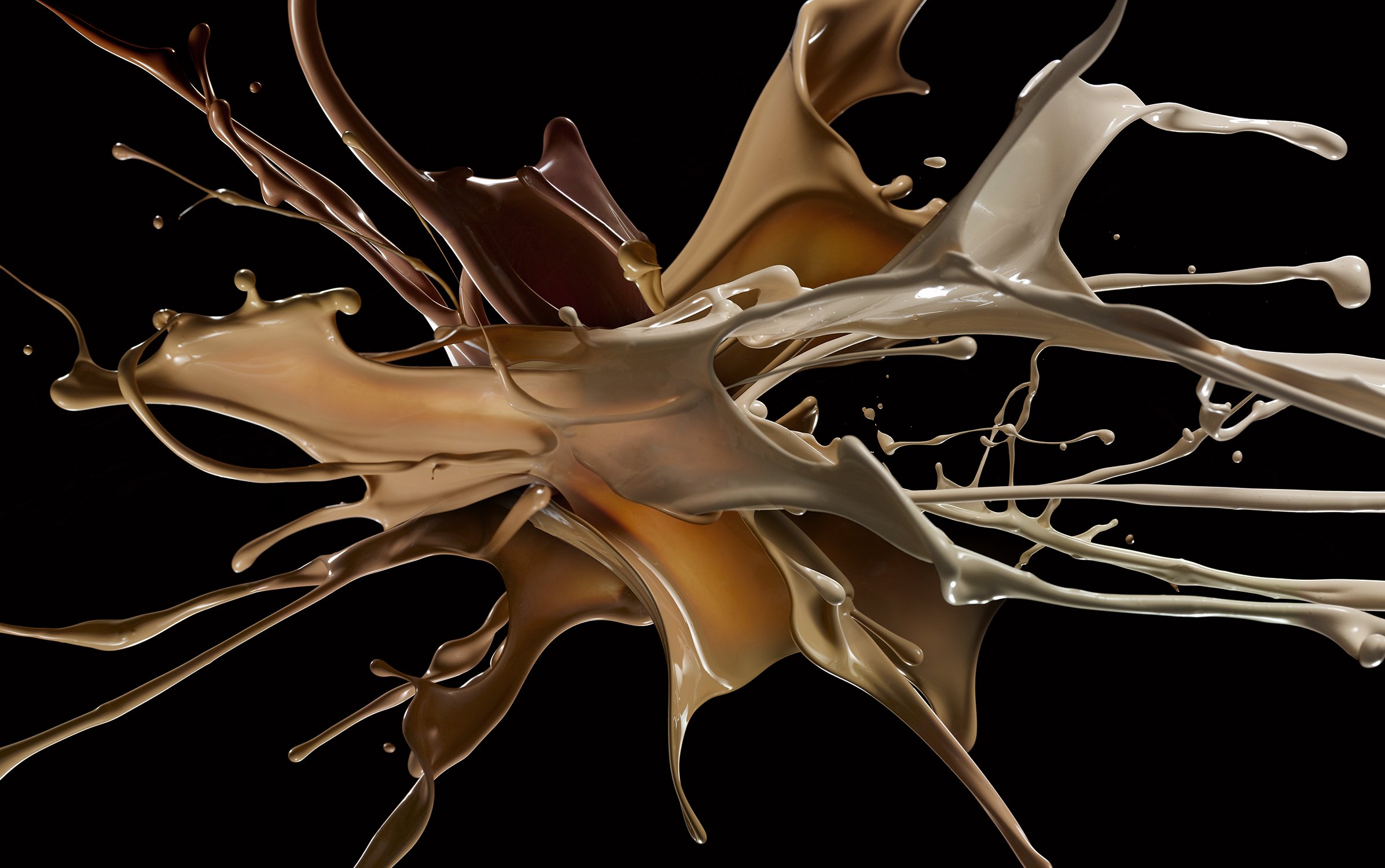 Abstract image of liquid caramel, chocolate, and cream colliding on a black backdrop creating a dynamic explosion of color and texture.