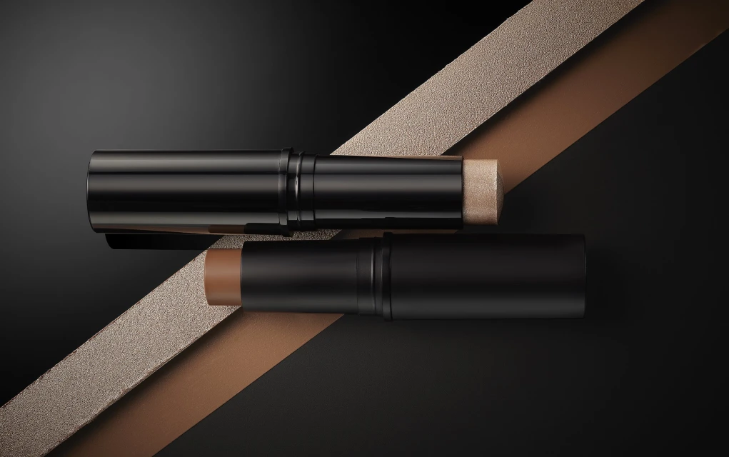 Two makeup contour sticks in black tubes are displayed against a dark background, with a textured ribbon adding depth to the composition.