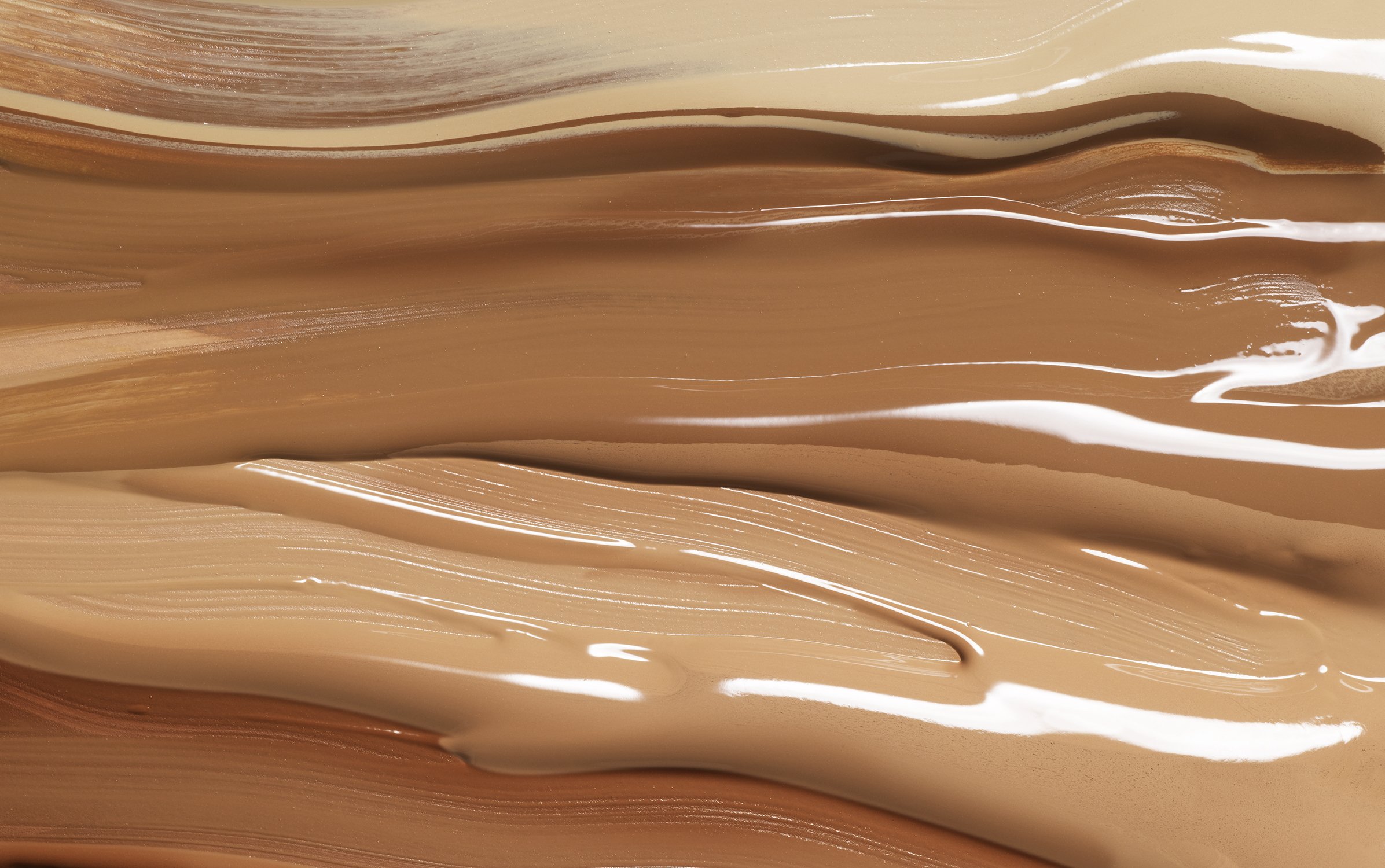 Close-up of multiple shades of liquid foundation swatches, ranging from light to dark tan, displaying textures and tones.