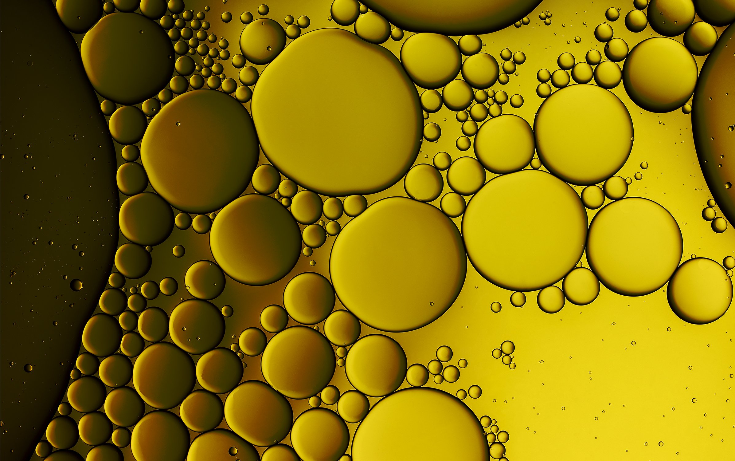 Golden-hued abstract image featuring numerous oil droplets of varying sizes clustered together, set against a soft yellow background.