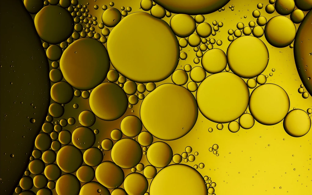 Golden-hued abstract image featuring numerous oil droplets of varying sizes clustered together, set against a soft yellow background.