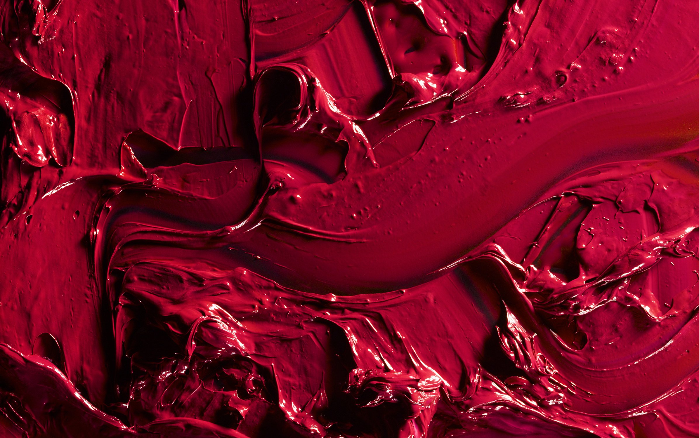 Close-up shot of thick, textured red paint creating an abstract design. The red paint has visible brushstrokes and glossy sheen.