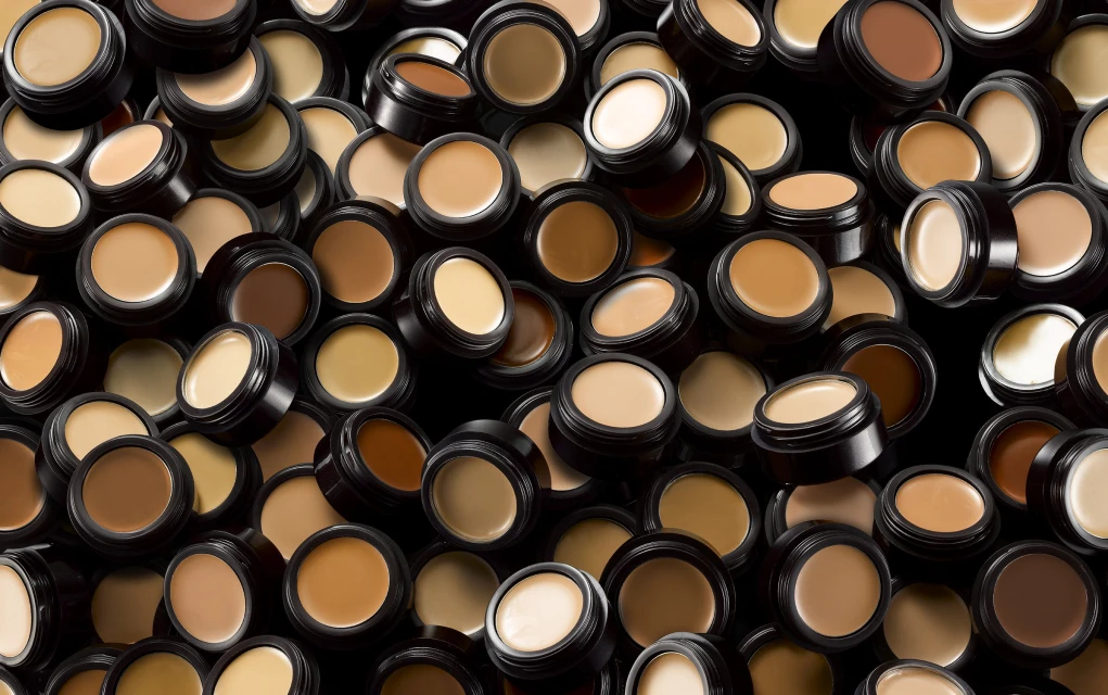 Multiple containers of makeup foundation shades are arranged against a dark background, creating a pattern for beauty and cosmetics.