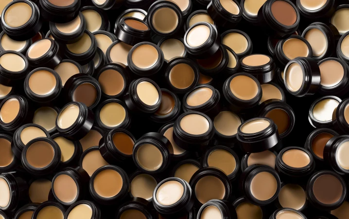 Multiple containers of makeup foundation shades are arranged against a dark background, creating a pattern for beauty and cosmetics.